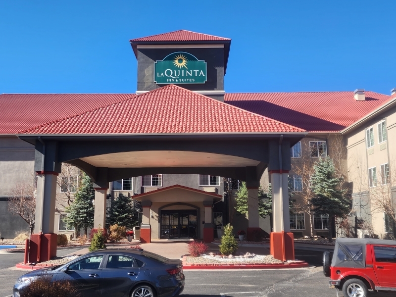 Exterior view of La Quinta Inn & Suites with red roof, large entrance canopy, and visible parking area with cars.