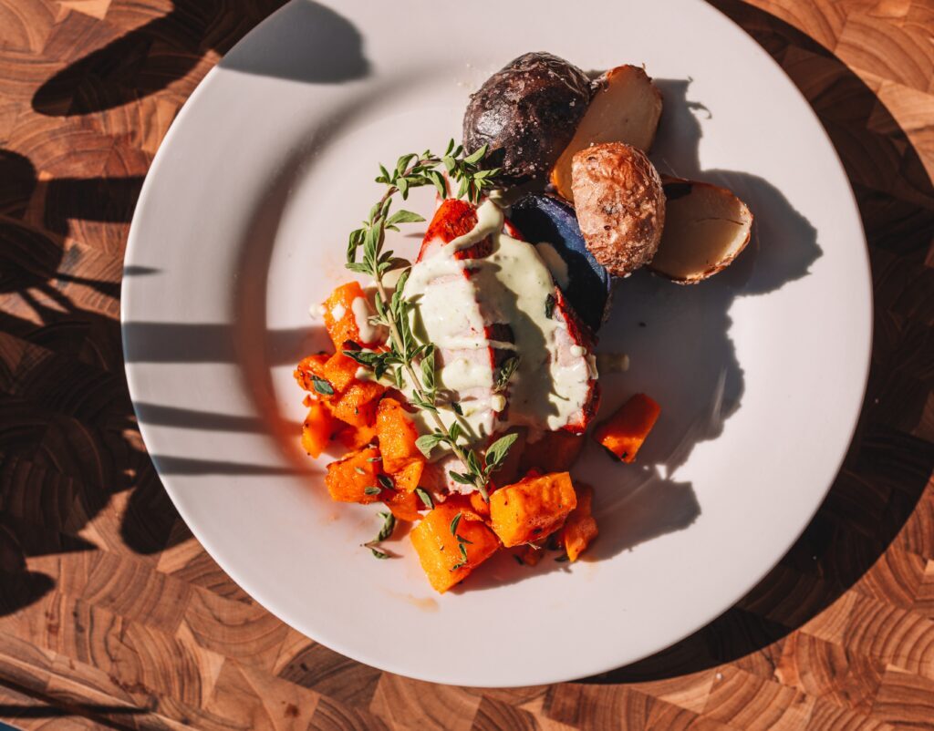 A plate of roasted potatoes, cubed squash, and a dish topped with creamy sauce, garnished with herbs.