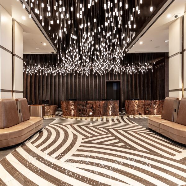 A modern, luxurious lobby with patterned flooring, brown couches, and an intricate chandelier installation hanging from the ceiling.